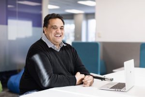 Dan wearing a dark jersey seated at the table, with his cane and laptop on the table.