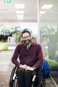 Matt wearing maroon business shirt seated in a wheelchair.