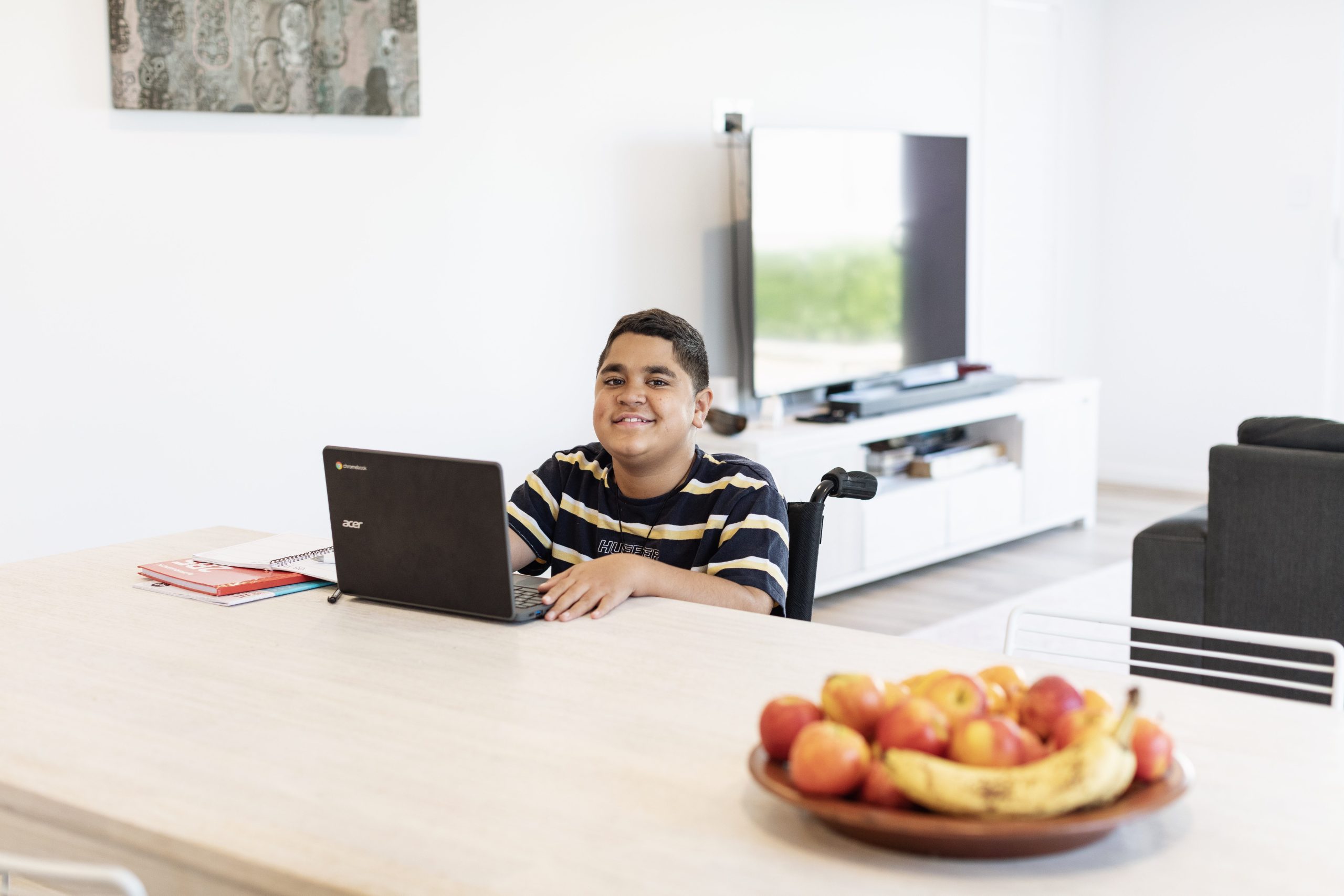 A young boy in striped shirt seated at the dinner table with an open laptop.