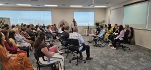 Team members are seated while new joiners stand at the front with their support people, replicating the whakawhānaungatanga form — the traditional format where men stood at the front and women at the back.