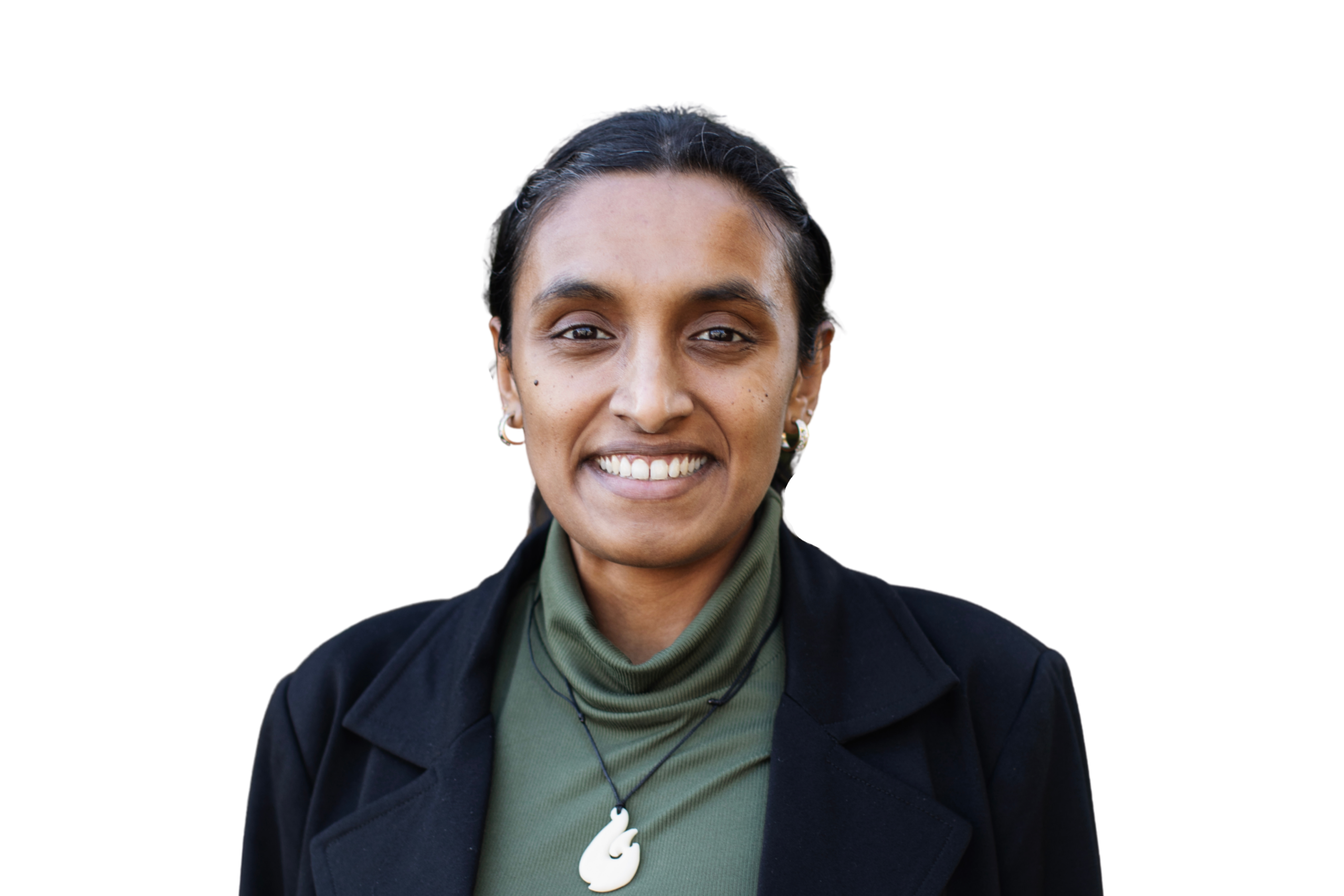 Kavindi has black hair that is tied back. She is wearing a green turtle neck top and black blazer. She is wearing a pounamu necklace.