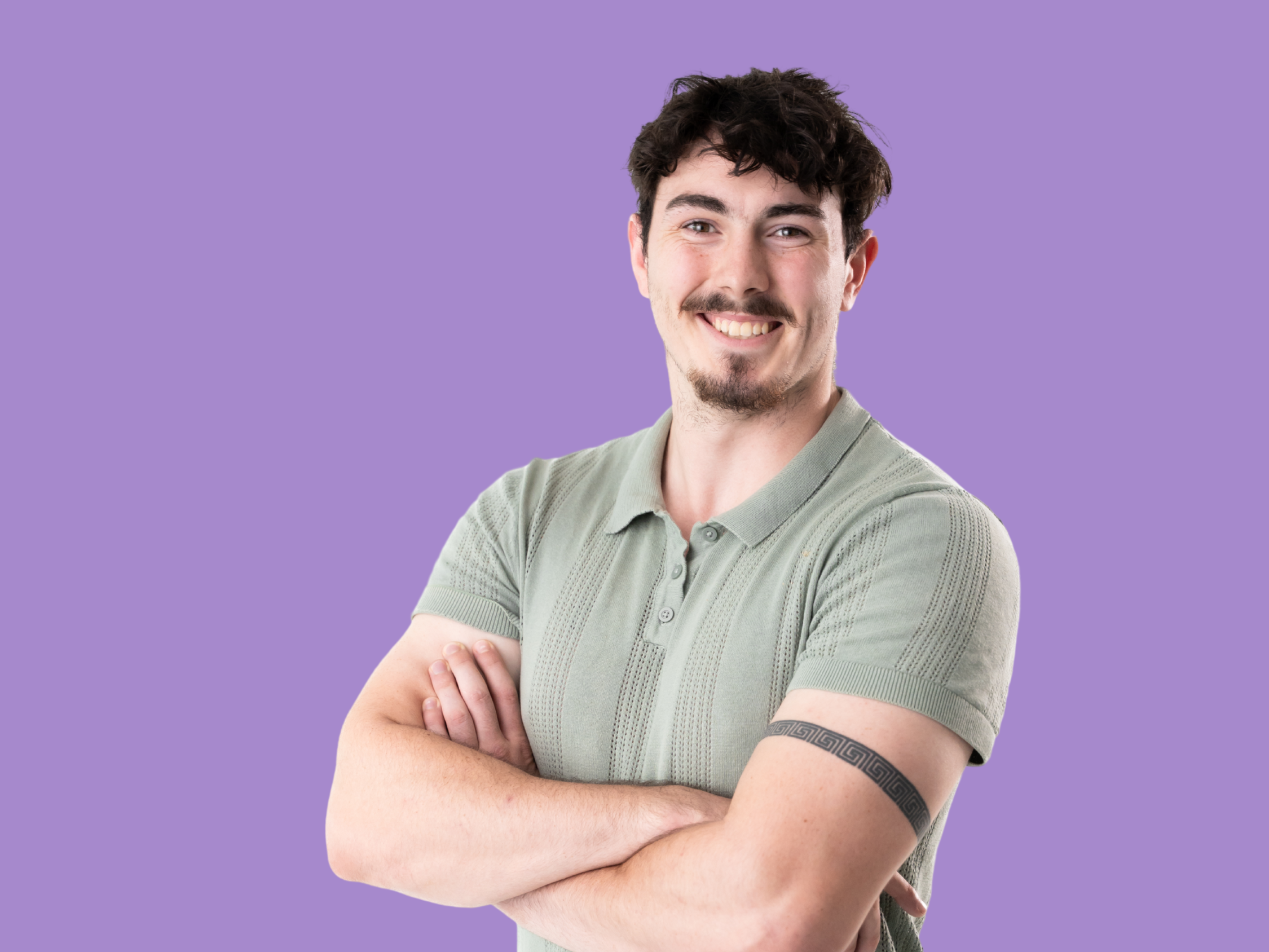 Luke is a young man with wavy black hair, wearing a green top and cream pants. He has facial hair and a tattoo on his right arm.