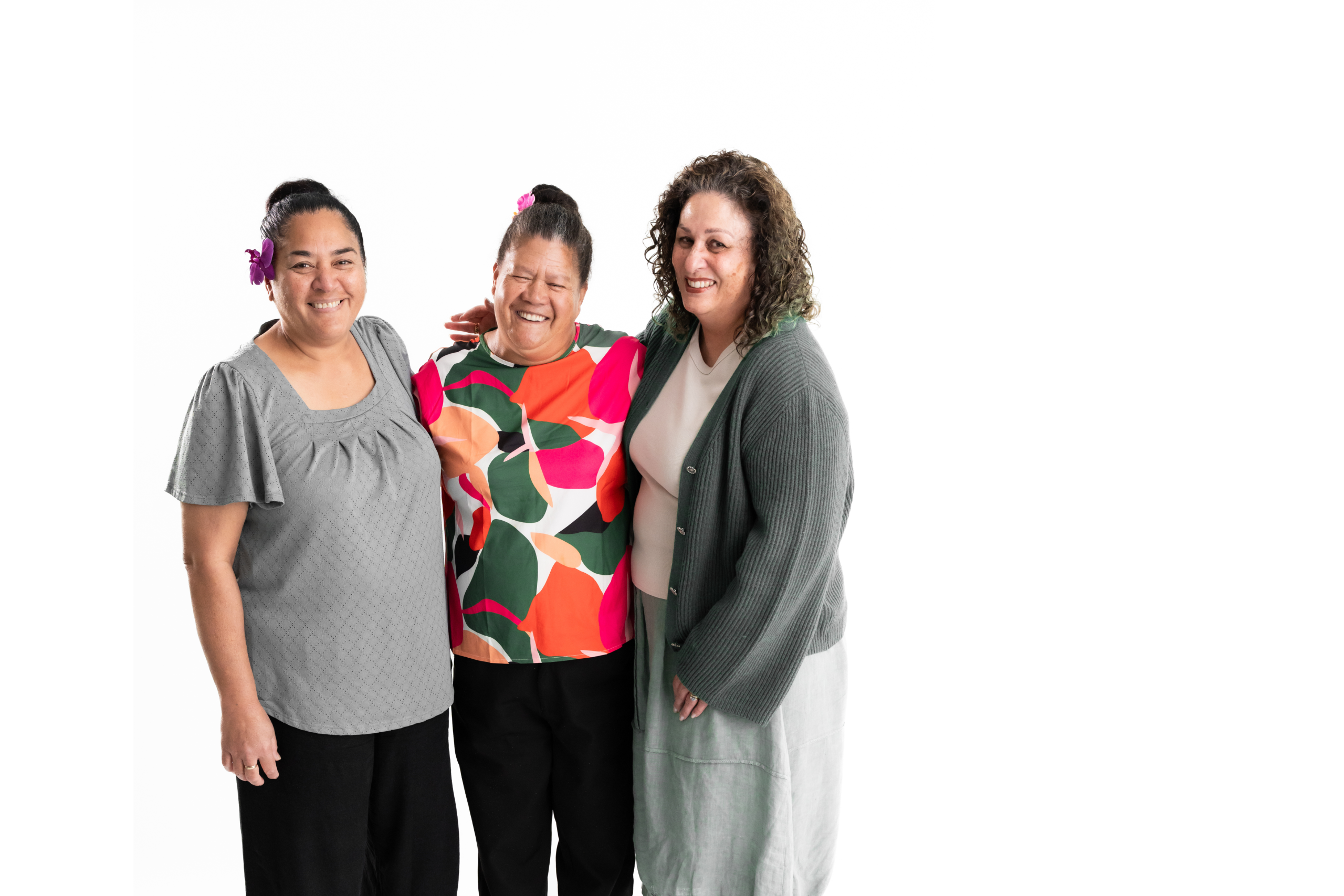 Three of our female employees standing closely together and smiling happily at the camera. They have Pacific and Maori ancestry, and are wearing shades of green.